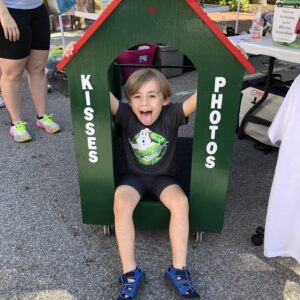 A boy sitting in a green house with kisses and photos written on it.