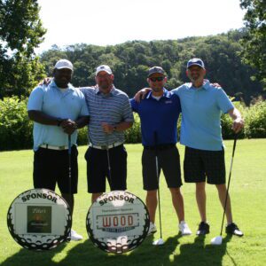 Four men standing on a golf course holding clubs.