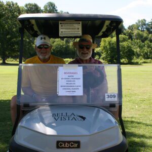 Two men in a golf cart on the grass.