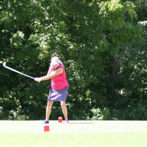 A woman swinging at a ball with a stick.