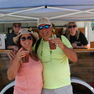 A man and woman holding drinks under an umbrella.