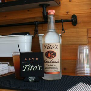 A bottle of tito 's vodka and some cups on the table.