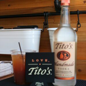 A bottle of tito 's vodka and a glass on the table.