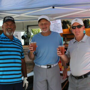 Three men holding drinks under a tent.